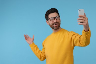 Photo of Smiling man taking selfie with smartphone on light blue background, space for text