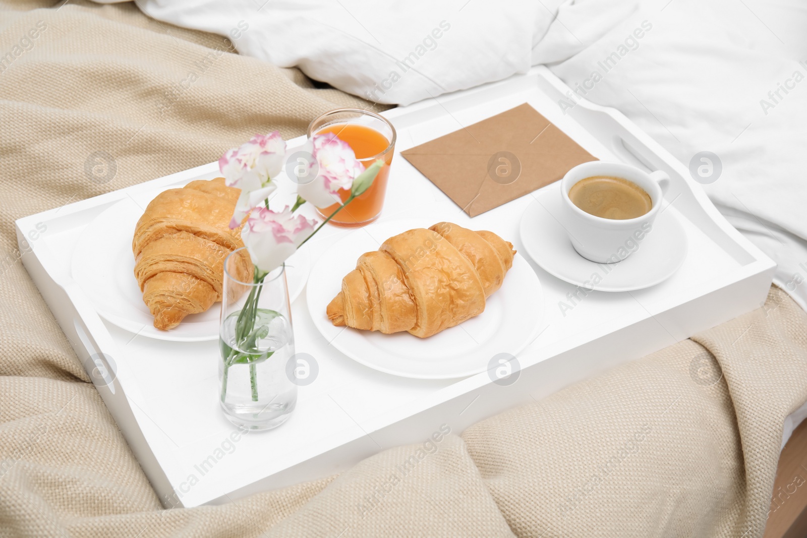 Photo of Tray with tasty croissants, drinks and flowers on bed