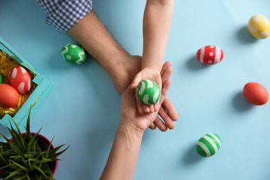 Photo of Father, mother and their child holding painted Easter egg on color background, top view