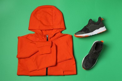 Photo of Orange hoodie and sport shoes on green background, flat lay