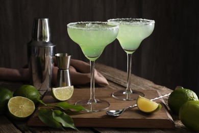 Photo of Delicious Margarita cocktail in glasses, limes and bartender equipment on wooden table