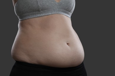 Woman with excessive belly fat on grey background, closeup. Overweight problem