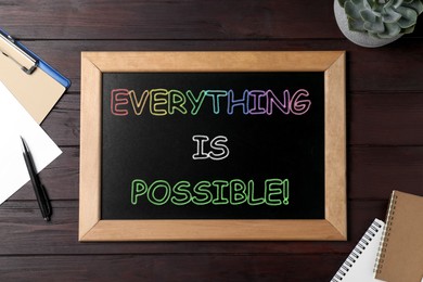 Small chalkboard with motivational quote Everything is possible, plant and stationery on wooden table, flat lay