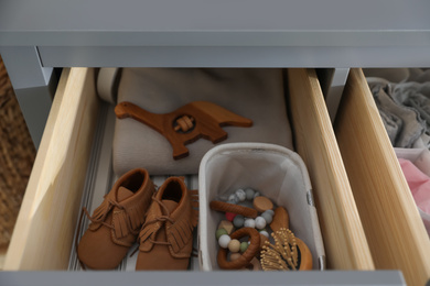 Photo of Open cabinet drawer with baby shoes and accessories in child room