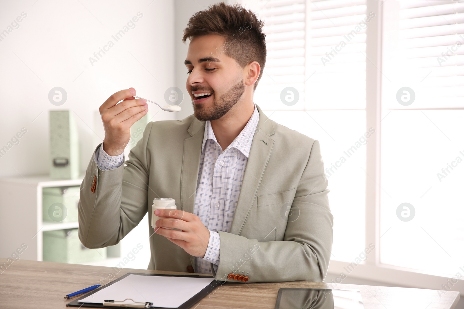 Photo of Happy young man eating tasty yogurt in office