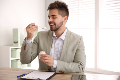 Happy young man eating tasty yogurt in office