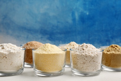 Bowls with different types of flour on table against color background. Space for text