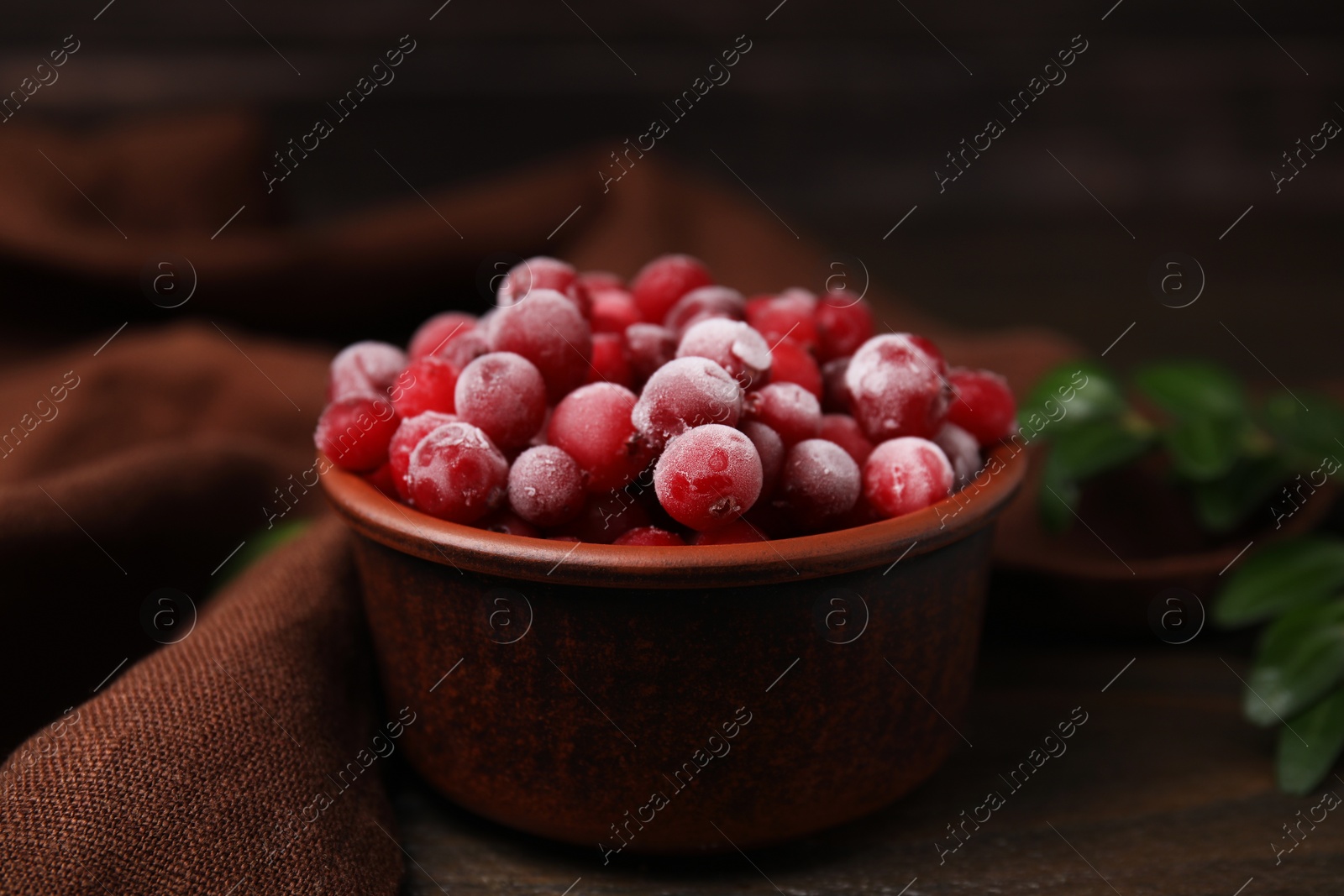 Photo of Frozen red cranberries in bowl on wooden table, closeup
