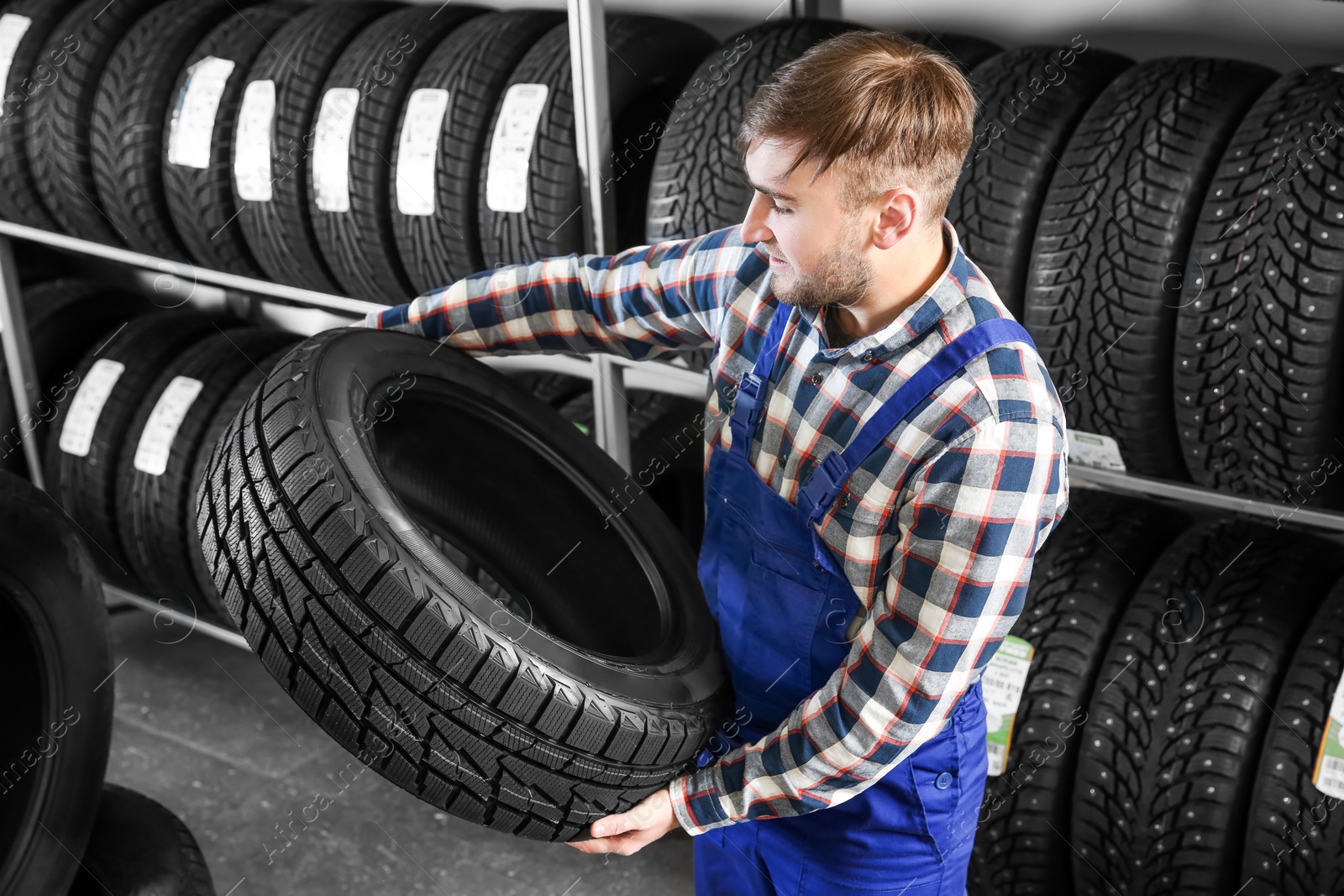 Photo of Young male mechanic with car tire in automobile service center