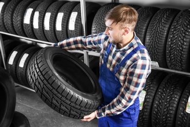 Young male mechanic with car tire in automobile service center