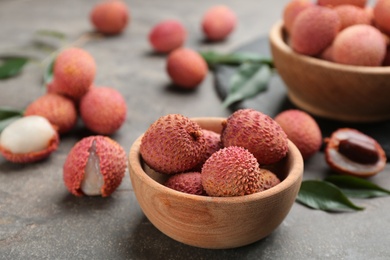 Photo of Fresh ripe lychee fruits in bowl on grey table. Space for text