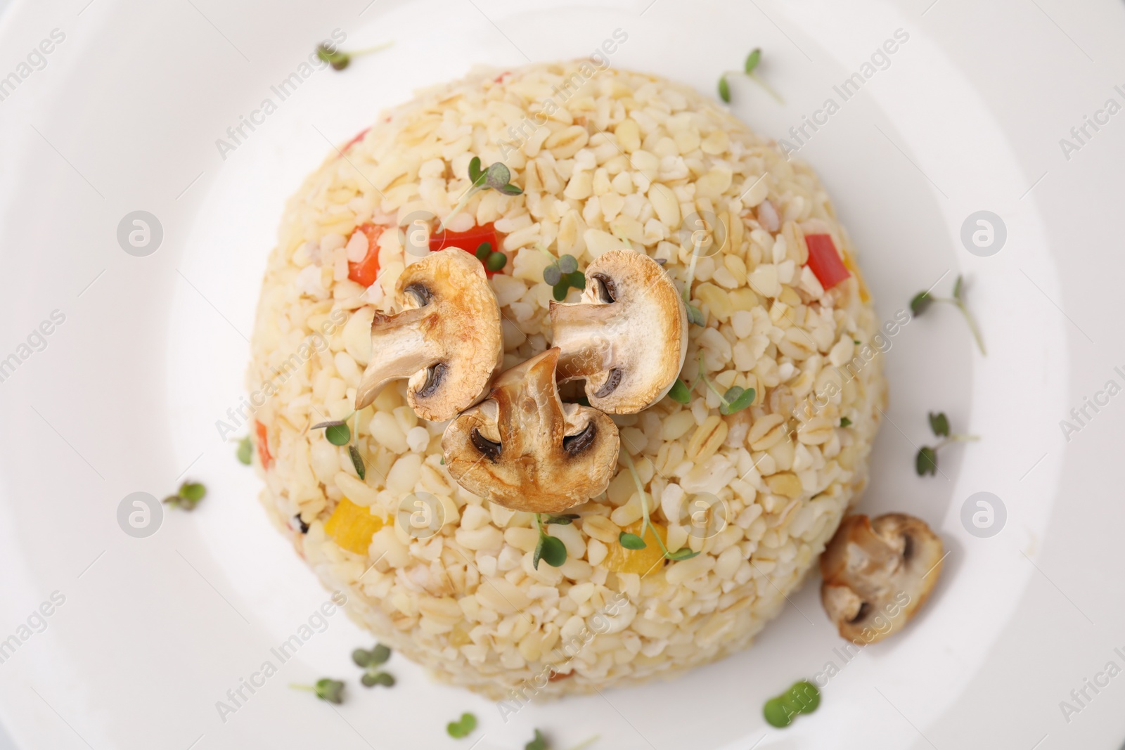 Photo of Delicious bulgur with vegetables, mushrooms and microgreens on plate, top view