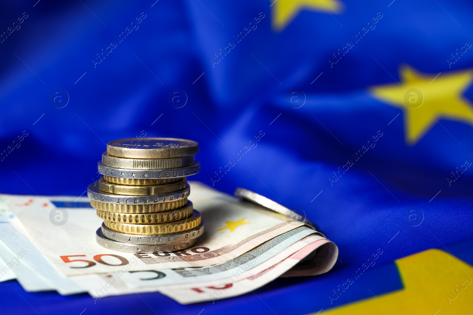 Photo of Stack of coins and banknotes on European Union flag, closeup. Space for text