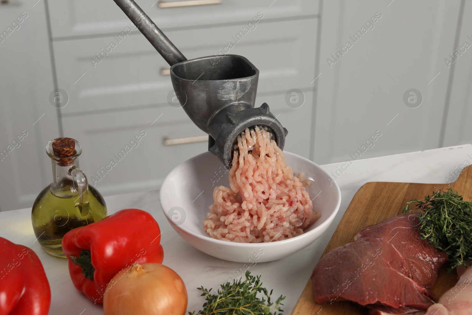 Photo of Metal meat grinder with chicken mince and products on white marble table in kitchen