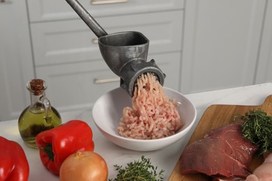 Metal meat grinder with chicken mince and products on white marble table in kitchen