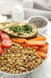 Delicious lentil bowl with avocado, tomatoes and carrots on white marble table