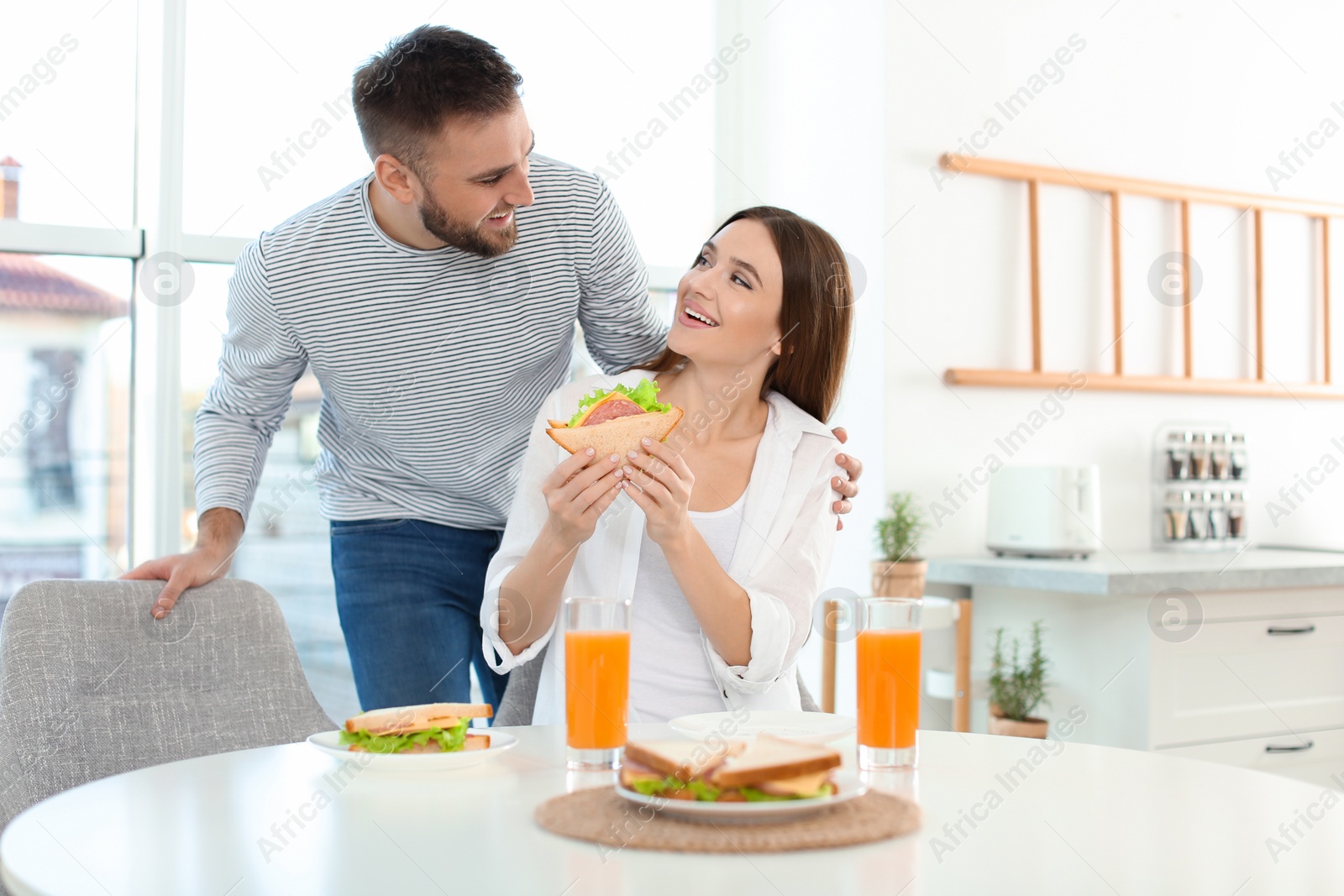 Photo of Happy couple having breakfast with sandwiches at table in kitchen