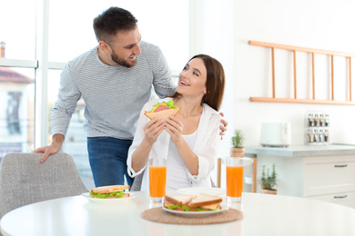 Happy couple having breakfast with sandwiches at table in kitchen