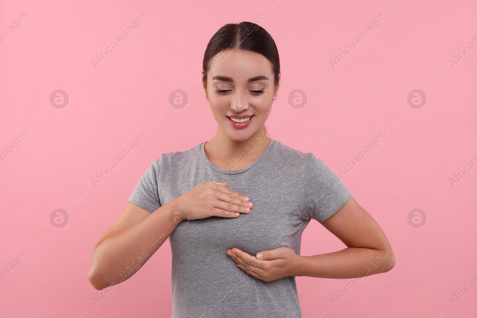 Photo of Beautiful young woman doing breast self-examination on pink background