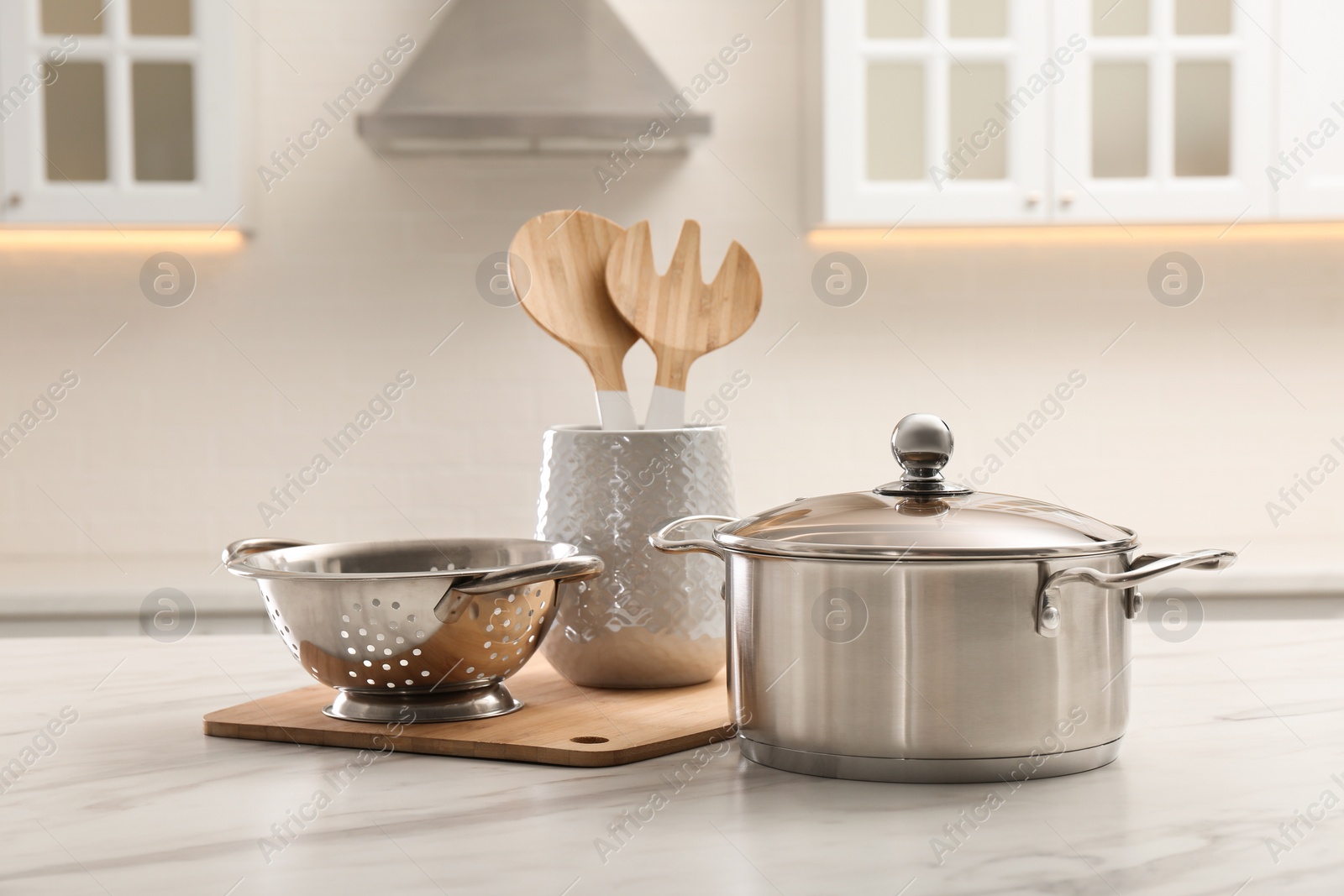 Photo of Pot, colander and kitchen utensils on white table indoors