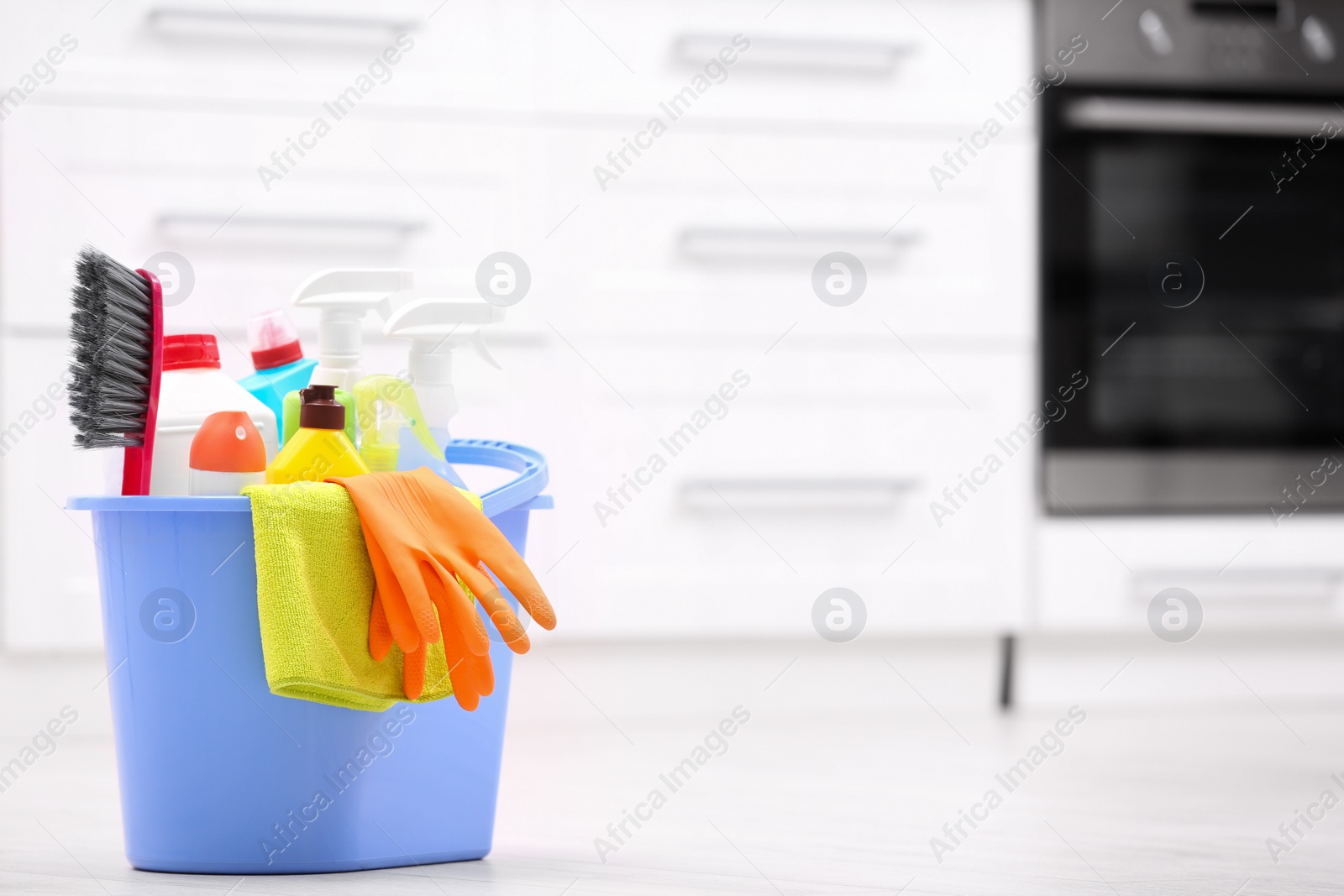 Photo of Bucket with cleaning supplies on floor in kitchen. Space for text