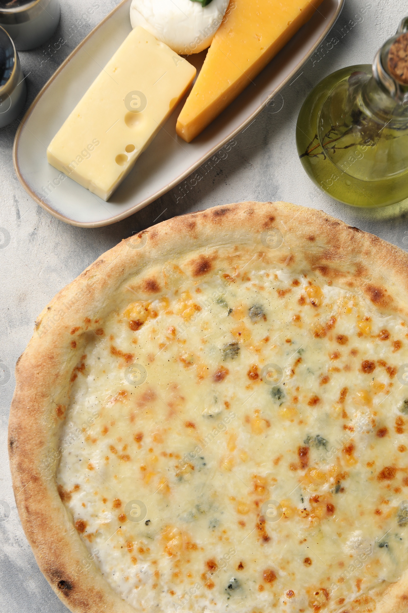 Photo of Delicious cheese pizza, oil and different kinds of cheese on light grey textured table, flat lay