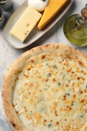 Photo of Delicious cheese pizza, oil and different kinds of cheese on light grey textured table, flat lay