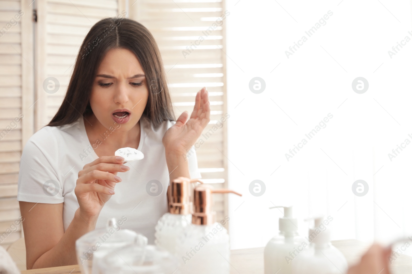 Photo of Beautiful woman holding cotton pad with fallen eyelashes near mirror indoors