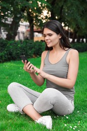 Photo of Young woman using smartphone on green grass in park