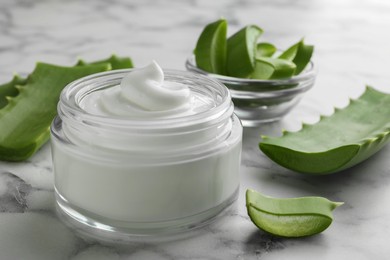 Jar with cream and cut aloe leaves on white marble table, closeup