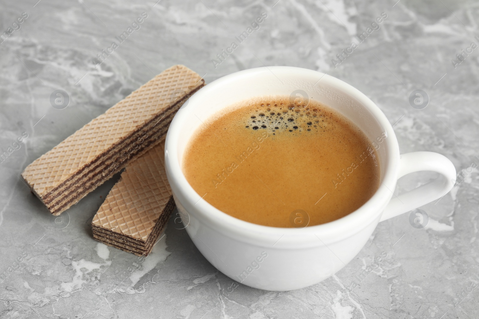 Photo of Delicious wafers and cup of coffee for breakfast on grey marble table