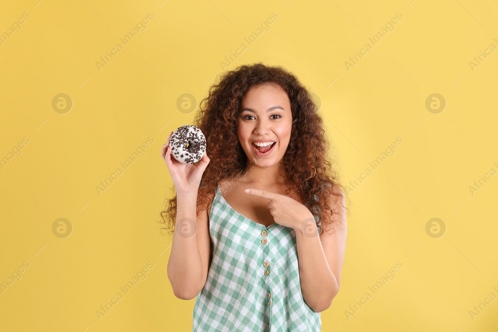 Photo of Beautiful African-American woman with donut on yellow background