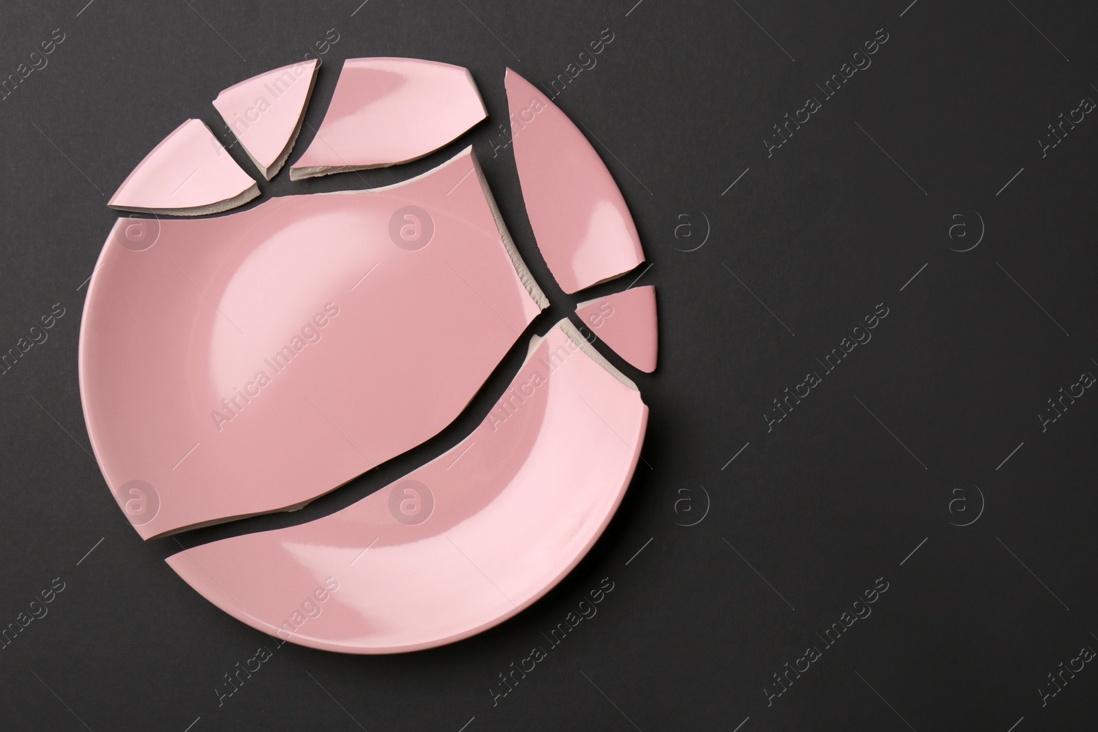 Photo of Pieces of broken pink ceramic plate on dark grey background, top view. Space for text