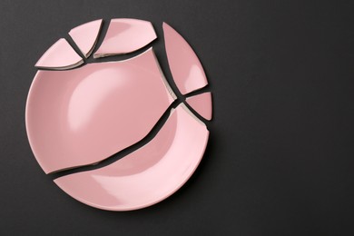 Photo of Pieces of broken pink ceramic plate on dark grey background, top view. Space for text