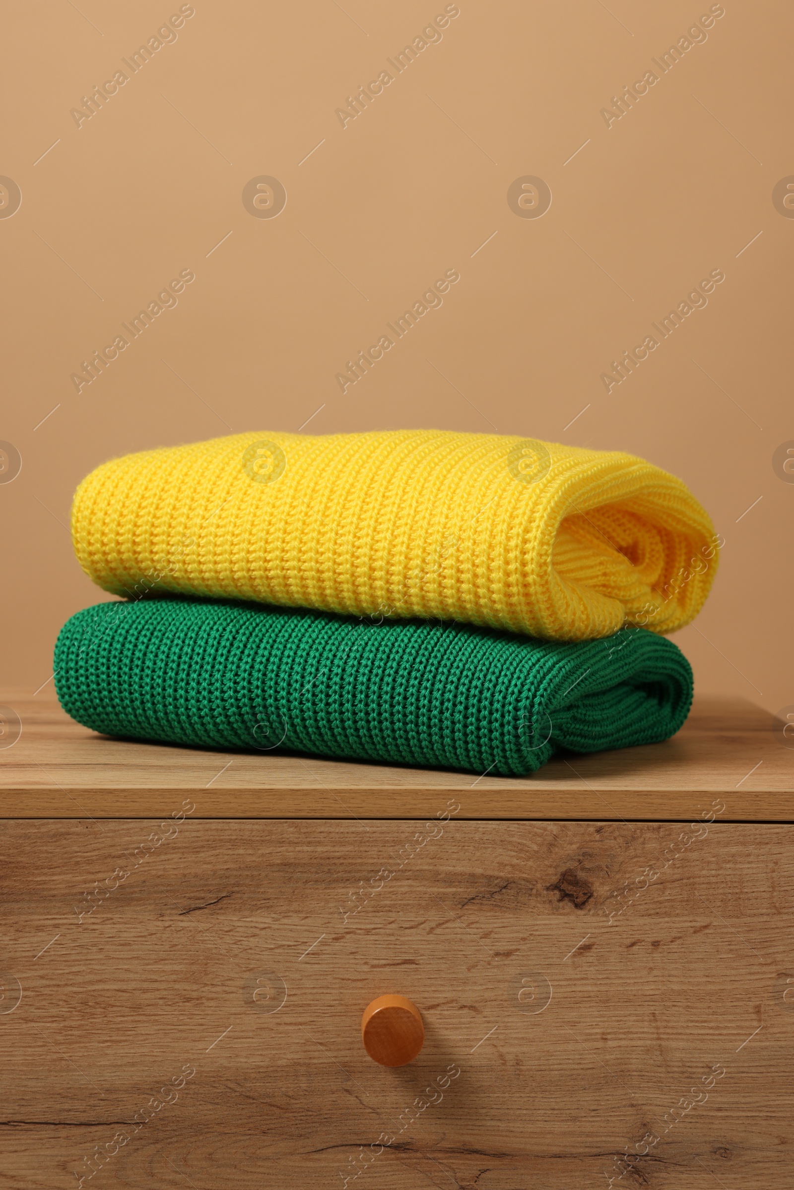 Photo of Different casual sweaters on chest of drawers against light brown background