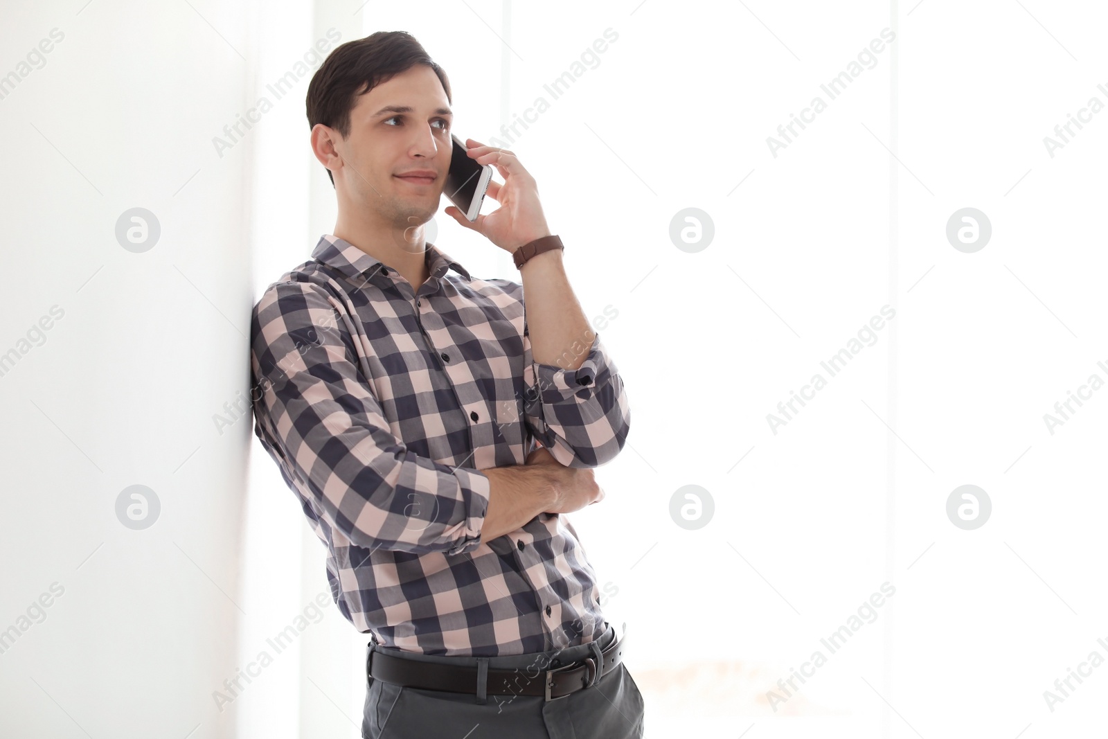 Photo of Portrait of confident young man with mobile phone near wall, indoors