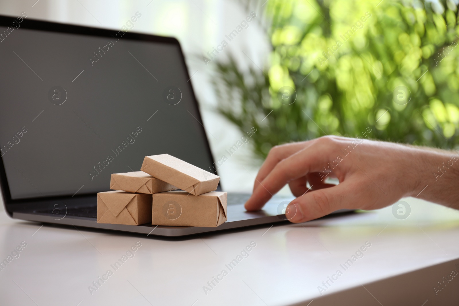 Photo of Internet shopping. Small boxes near man using laptop at table indoors, closeup