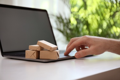 Internet shopping. Small boxes near man using laptop at table indoors, closeup