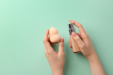 Woman with makeup sponge and skin foundation on mint color background, top view. Space for text