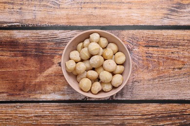 Photo of Delicious peeled Macadamia nuts in bowl on wooden table, top view