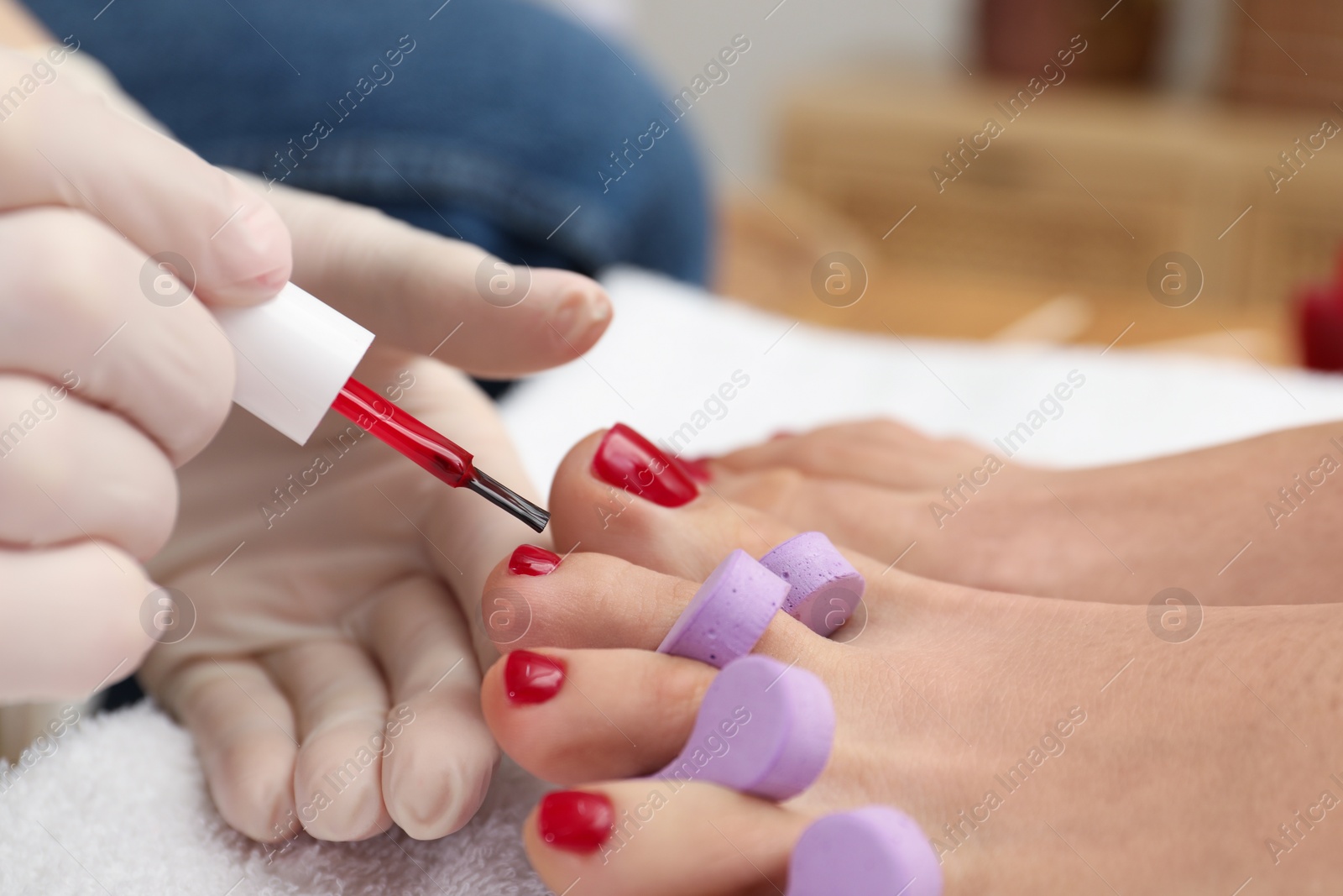 Photo of Pedicurist painting client`s toenails with red polish in beauty salon, closeup