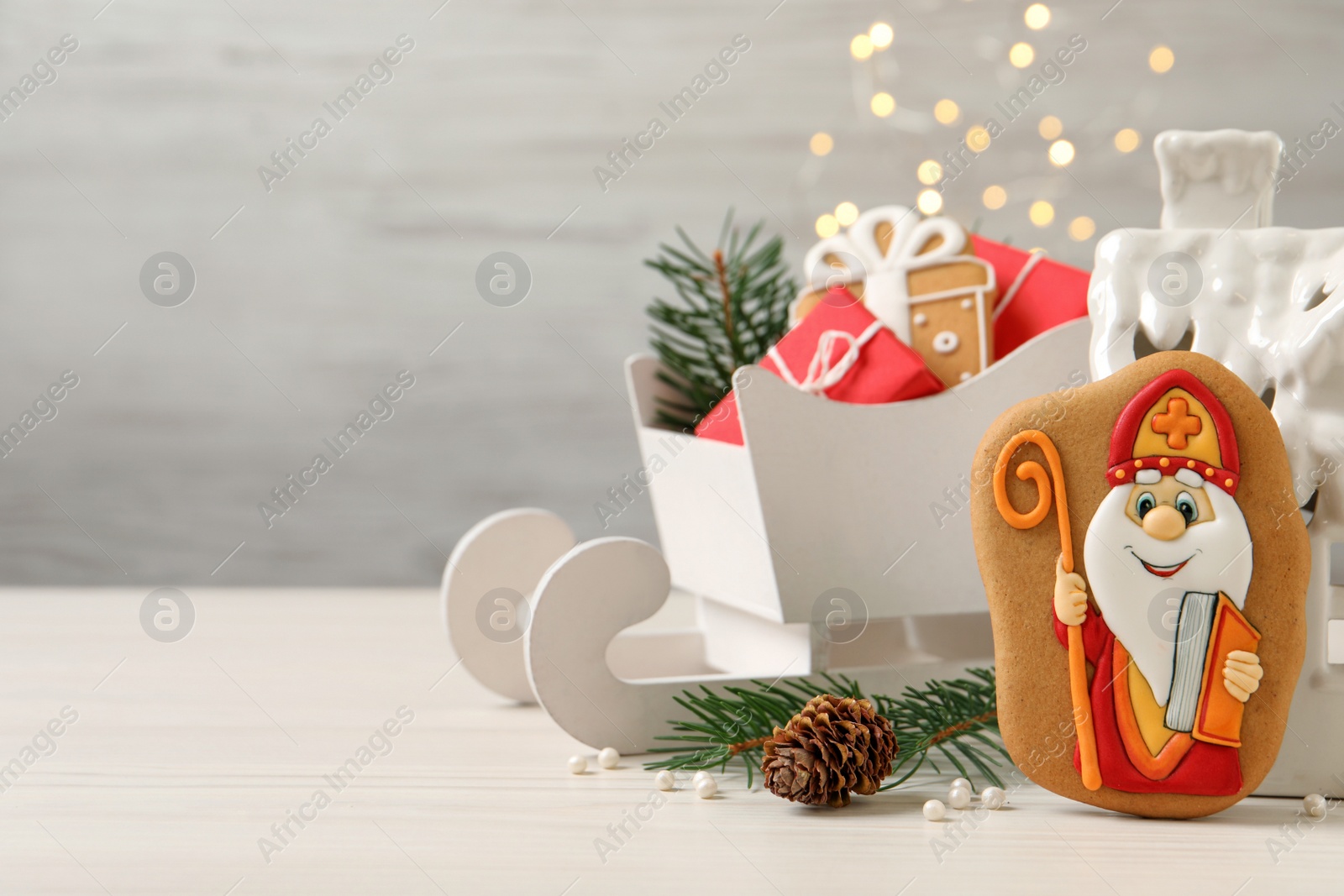 Photo of Composition with tasty gingerbread cookies on white wooden table against blurred lights, space for text. St. Nicholas Day celebration