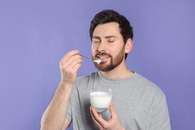 Photo of Handsome man eating delicious yogurt on violet background