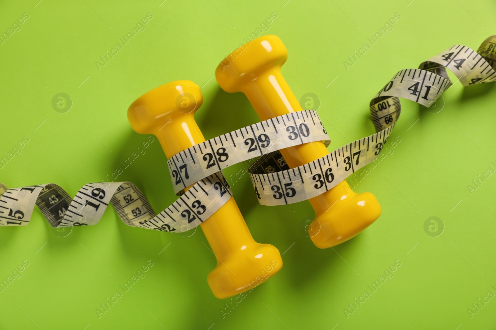 Photo of Measuring tape and dumbbells on light green background, flat lay. Weight control concept