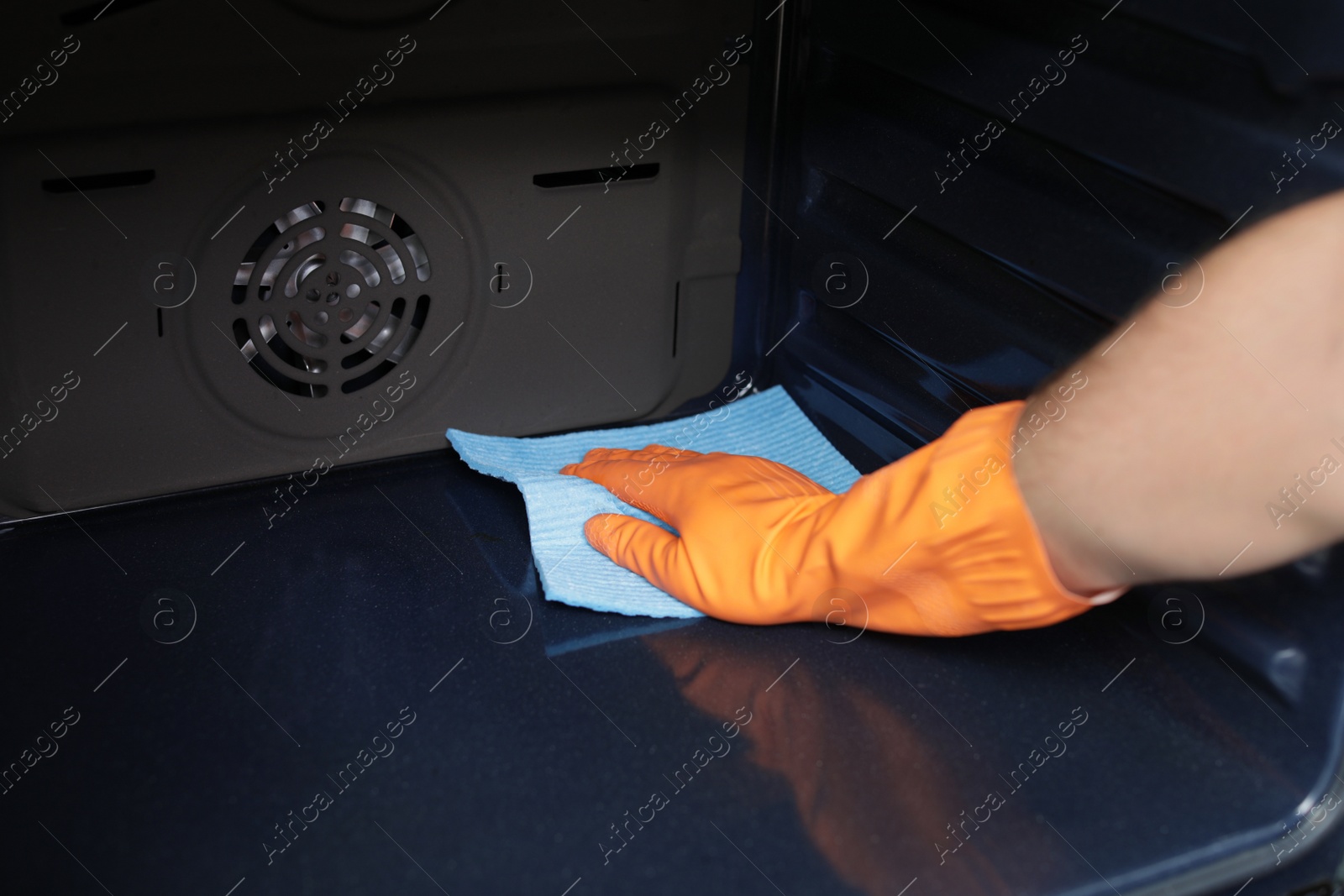 Photo of Young man cleaning oven with rag in kitchen, closeup