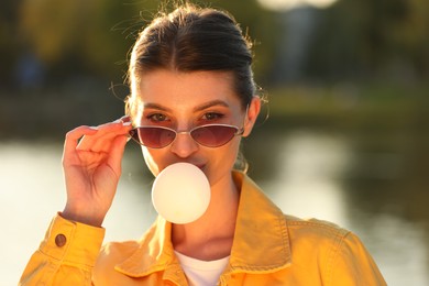 Photo of Beautiful young woman in sunglasses blowing bubble gum outdoors