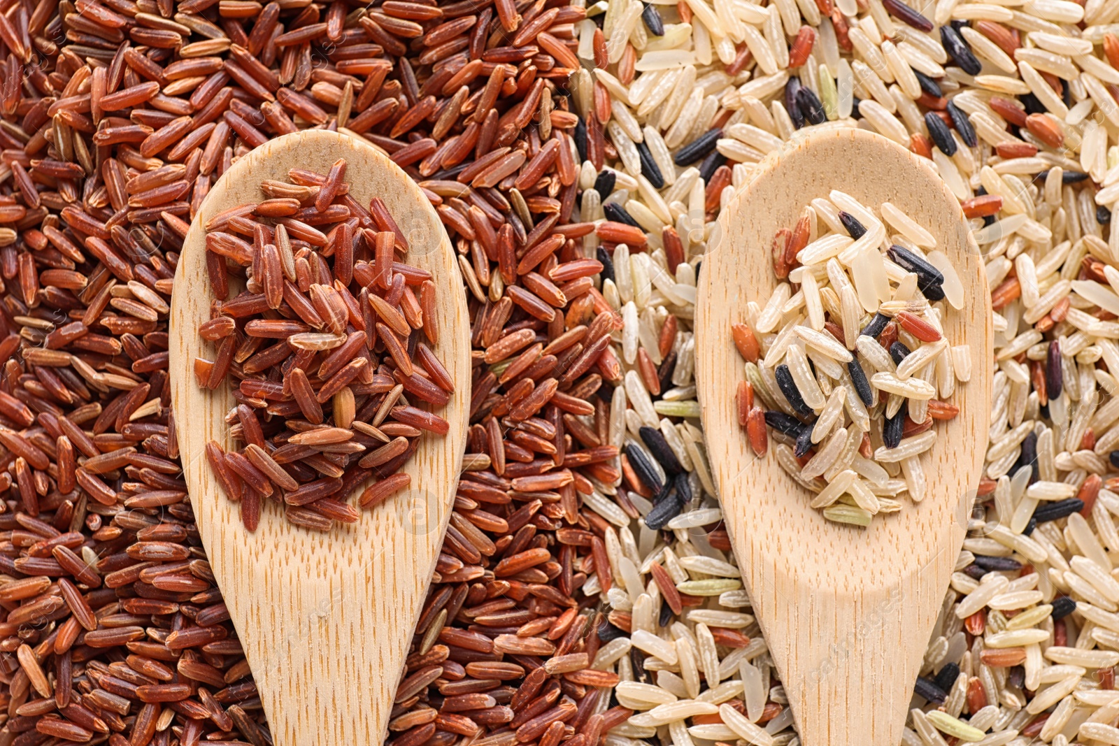 Photo of Pile of different brown rice with wooden spoons, flat lay