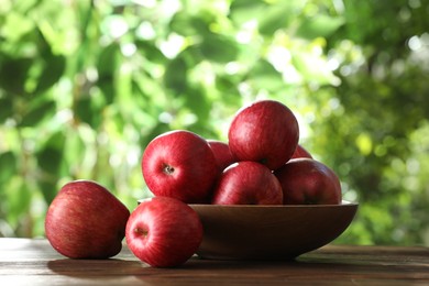 Photo of Ripe red apples and bowl on wooden table outdoors