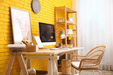 Stylish home office interior with comfortable workplace near yellow brick wall