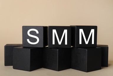 Photo of Black cubes with abbreviation SMM (Social media marketing) on beige background